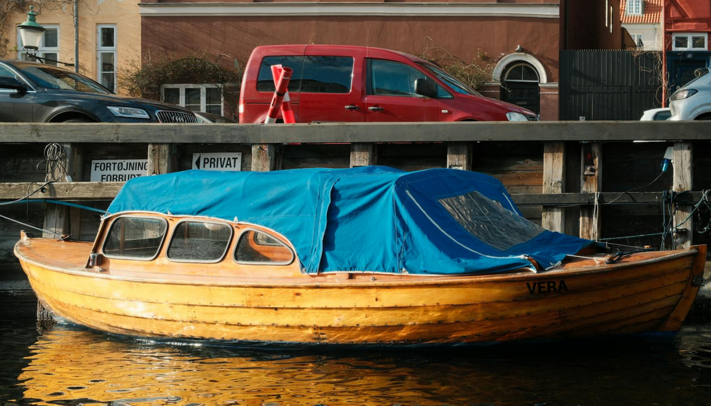 Wooden boat with blue cover docked in a canal next to urban architecture.