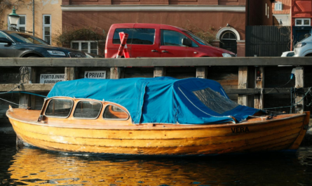 Wooden boat with blue cover docked in a canal next to urban architecture.