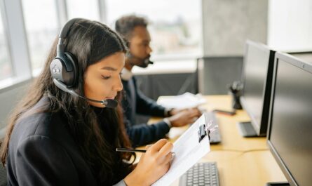 Two call center agents wearing headsets working at desks with computers in a modern office.